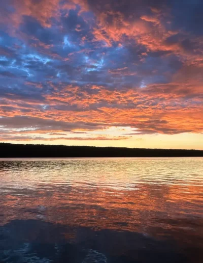 Vivid sunset over calm water with reflected orange and blue clouds.